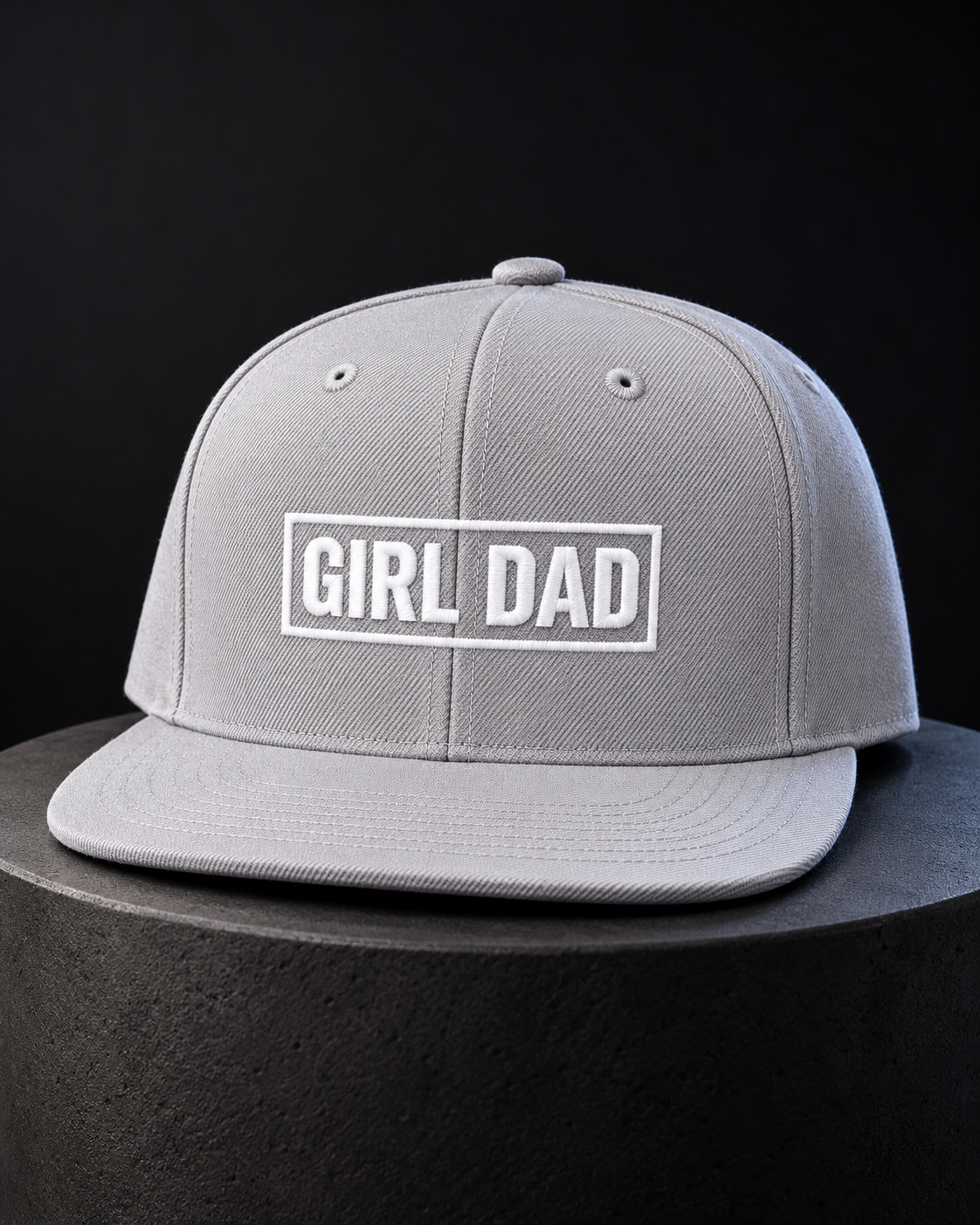 Gray GIRL DAD snapback cap with white raised embroidery photographed on a dark studio display