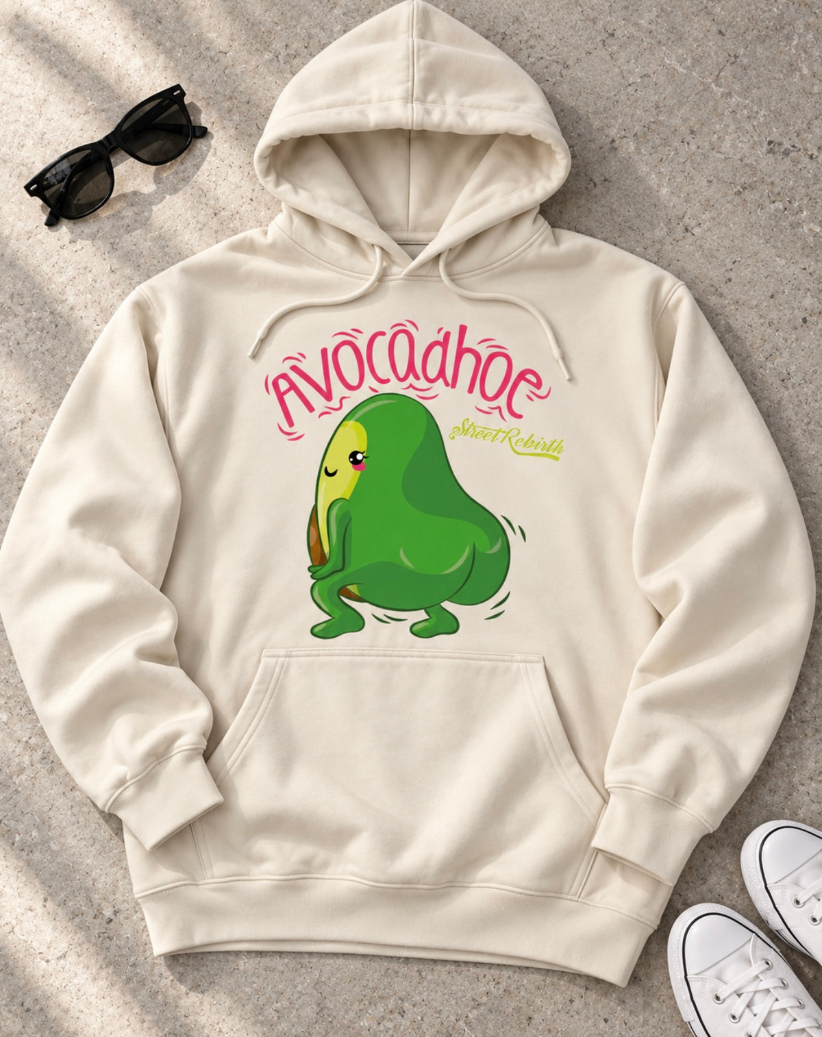 Cream pullover avocado pun hoodie flat lay on pale stone with sunglasses and sneakers