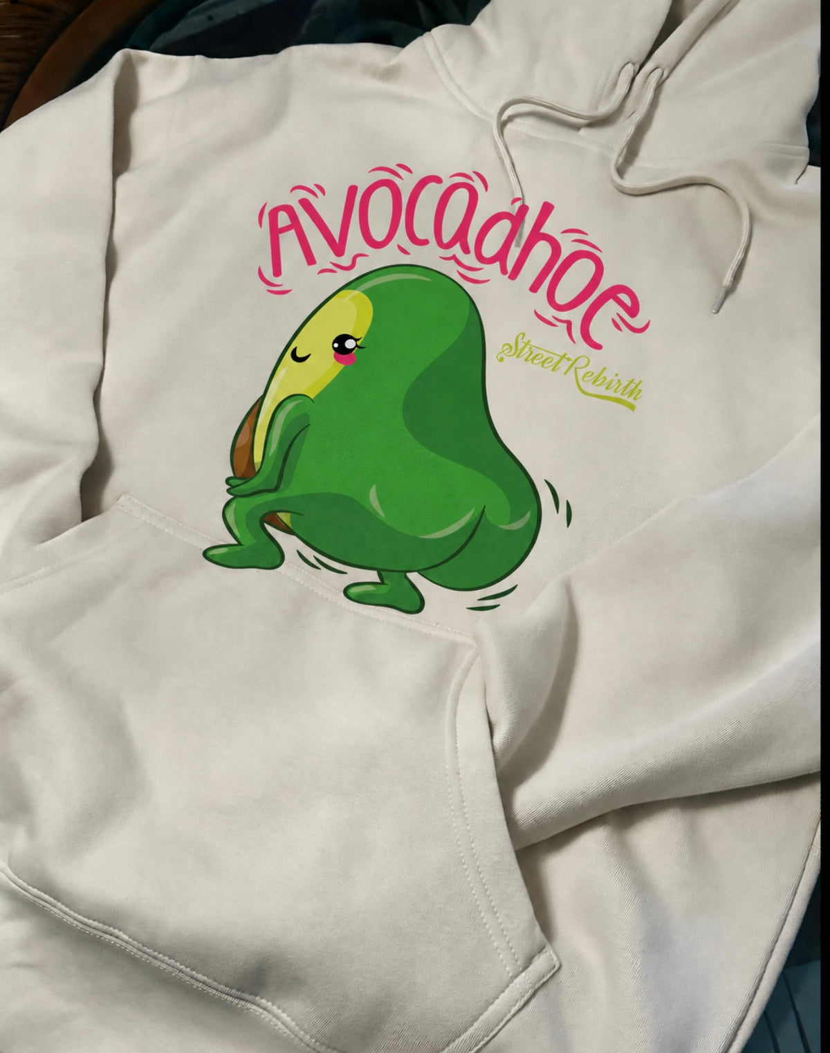 Close-up of pink Avocadhoe lettering and green cartoon avocado artwork printed on cream hoodie